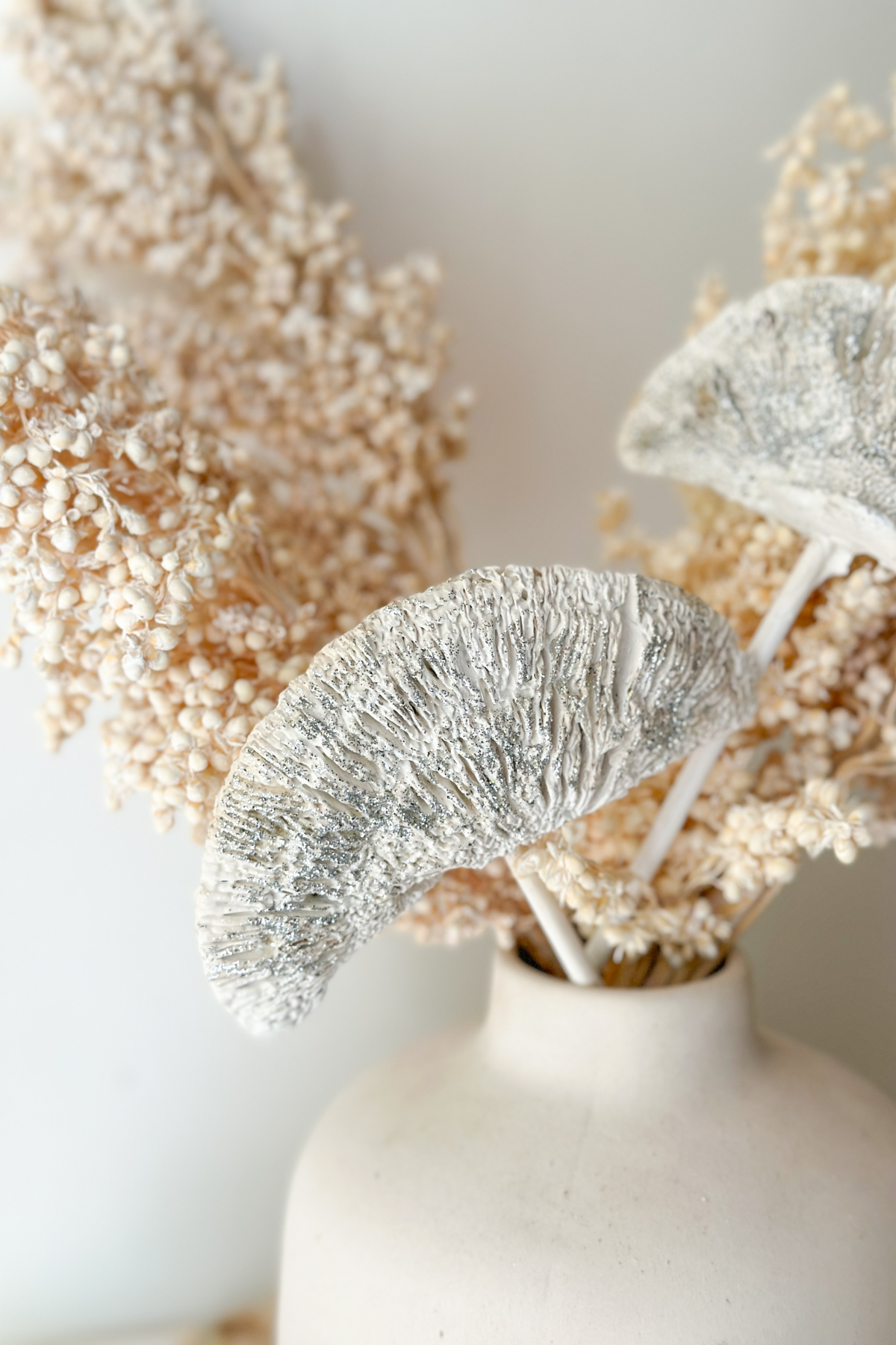 Decorative arrangement with silver glitter and beige flowers in a white vase on a light background