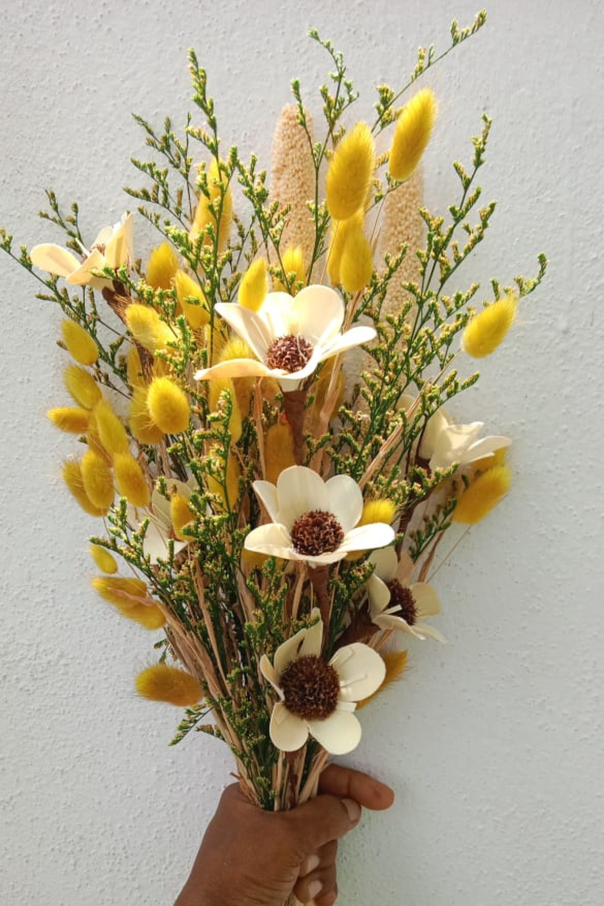 Bouquet of yellow and white flowers held against a light gray background